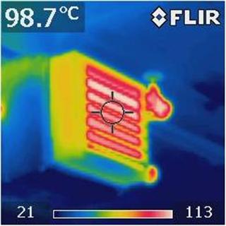 FLIR thermal image of a heating element glowing red and yellow, with a peak temperature reading of 98.7°C displayed in the corner.